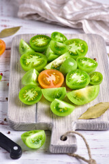 Green and red cut tomatoes on a gray board, side view, close-up.
