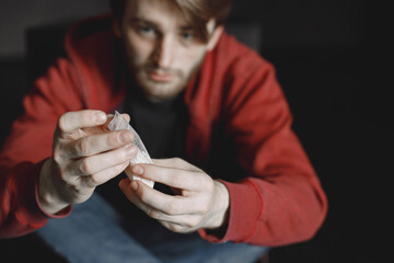 Young addicted man with cocain packet sitting alone