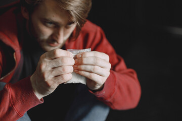 Young addicted man with cocain packet sitting alone