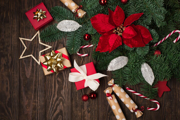 Holiday card - red flower poinsettia, Christmas decorations, gift boxes and candy canes on dark wooden background.