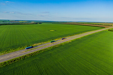 Obraz premium convoys with cargo. red green and blue trucks are driving on asphalt road along the green fields with goods. seen from the air. Aerial view landscape. drone photography.