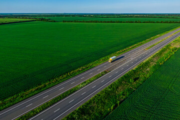yellow truck driving on asphalt road along the green fields. shipping goods, seen from the air. Aerial view landscape. drone photography. cargo delivery