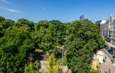 Scenic cityscape of Riga, Latvia. Top view of green trees in city park. Road with cars and modern architecture.