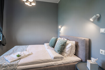 Modern interior in grey tones of bedroom. Queen size bed with pillows. Napkins on night table.