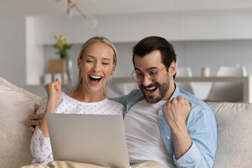 Joyful laughing young married family couple looking at laptop screen, feeling excited of reading amazing online lottery gambling betting auction win, supporting favorite team watching sport match.