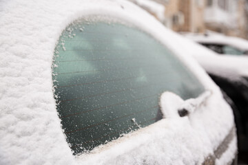Snow suddenly fell on cars and roads. A car wiper cleans the rear glass from a thick layer of snow. Road safety. Selective focus