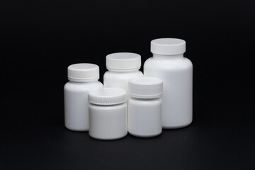 White plastic pill jars on a black background. Isolated