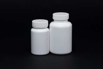 White plastic pill jars on a black background. Isolated