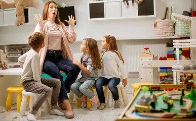 Nursery teacher talking story to group of children sitting on a chairs at kindergarten