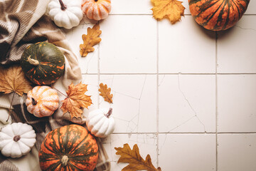 Cozy autumn flat lay with pumpkins, plaid and autumn leaves on tile background. Autumn home decor. Cozy fall mood. Thanksgiving. Halloween.