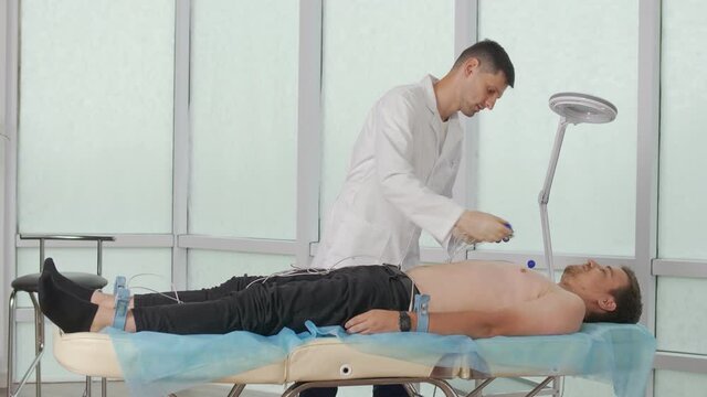 Electrocardiogram Procedure for Diagnosing Heart Disease. A Cardiologist Puts Electrodes on the Bare Chest of a Young Man Lying on the Couch To Take an Electrocardiogram in the Clinic'S Office.