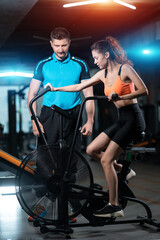 female has workout and training on exercise bike with personal trainer in gym