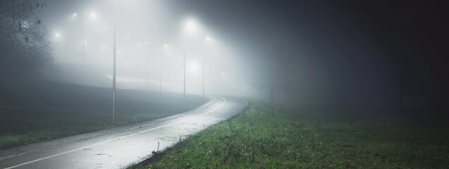 An empty illuminated bicycle road with a sharp turn in a fog at night. Lanterns close-up. Bridge in...