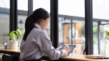 Asian woman hand holding pen stylus writing on digital tablet computer. close up