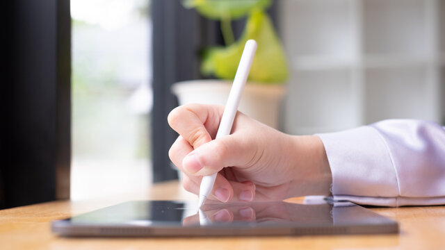 Asian Woman Hand Holding Pen Stylus Writing On Digital Tablet Computer. Close Up