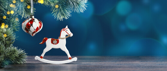 Christmas ornaments and gift boxes on green with snow. Rocking horse under Christmas tree. New Year greeting card. Copy space banner. Bokeh lights
