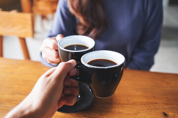 Closeup image of a man and a woman clinking coffee mugs in cafe