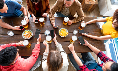 Top view of multiracial friends hands using smartphones - Men and girls sitting - Boys and girls sitting at a pub table using cellphones while drinking beer - Phone addiction concept of young people