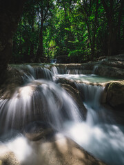 Scenic view of Erawan Waterfall. Closeup beautiful smooth flowing water with sunlight and emerald green pond in lush rainforest. Kanchanaburi, Thailand. Long exposure.