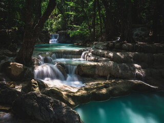 Naklejka na ściany i meble Scenic view of Erawan Waterfall. Breathtaking smooth flowing water with sunlight and emerald green pond in lush rainforest. Kanchanaburi, Thailand. Long exposure.