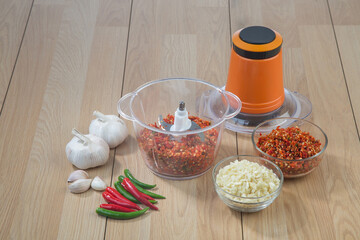 Food processor with chopped chili and garlic on wooden table background