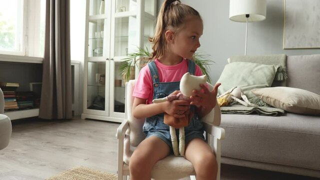Excited child in rocking chair playing with her stuffed toys while sitting in living room at home.