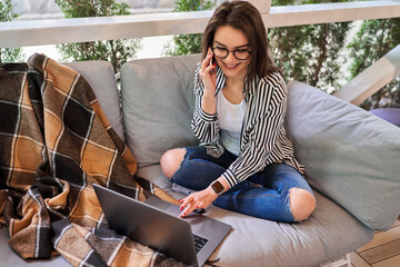 Beautiful student girl in glasses learn at home with laptop and speaking phone.