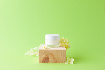 Fototapeta na wymiar Jar of cosmetic cream with wood podium and flowers on green background. Close up, copy space