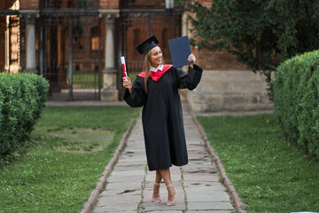 Portrait of woman on her graduation day in graduated robe with diploma in her hands