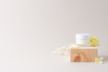 Jar of cosmetic cream with wood podium and flowers on grey background. Close up, copy space