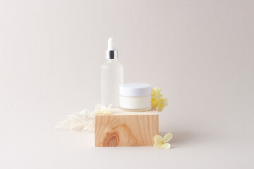 Cosmetic skin care products with wood podium and flowers on grey background. Close up, copy space