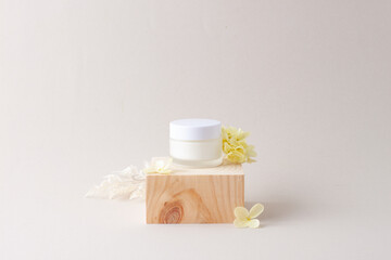 Fototapeta na wymiar Jar of cosmetic cream with wood podium and flowers on grey background. Close up, copy space