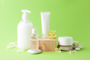 Cosmetic skin care products with wood podium and flowers, stone on green background. Close up, copy space