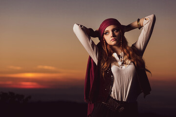 Outdoor portrait of young female in pirate costume, sunset behind.