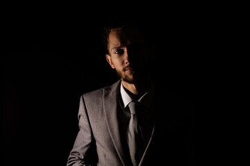 A young businessman in a smart gray suit looking at the camera with moody lighting that casts half of him into shadow