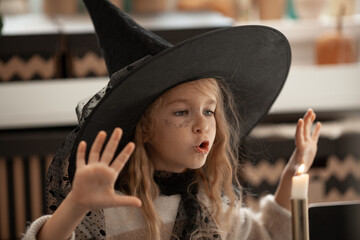 A girl in a witch hat conjures a candle, a child is dressed in a costume for a halloween party,...