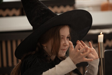 A girl in a witch hat conjures a candle, a child is dressed in a costume for a halloween party,...
