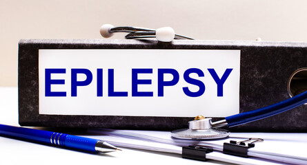 The desktop has a stethoscope, a blue pen, and a gray file folder with the text EPILEPSY. Medical...