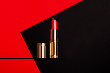Open bright red lipstick in gold and silver packaging stands on glass against a red and black...