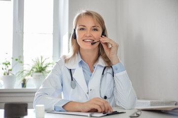 A smiling woman doctor with headphones and a microphone in a white coat conducts an online consultation. Ehealth services,medical internet technology apps,telehealth concept.