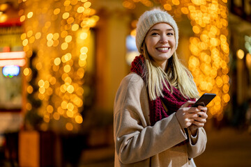 Portrait of beautiful young woman using her mobile phone in the street with christmas decoration.