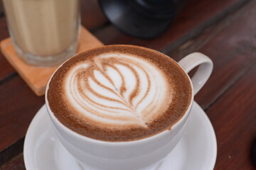 coffee latte art in the shop cafe. A new morning with coffee to eat to increase the workforce. Cup of cappuccino with art on wooden table. Latte art coffee in white cup with saucer on wooden table