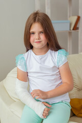 Naklejka premium Child with a cast on a broken wrist or arm smiling and having fun on a couch. Positive attitude, recovery and kid concept.