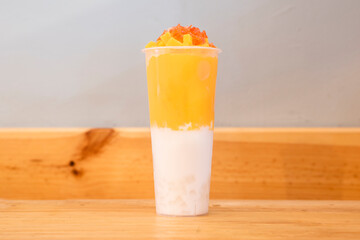 Mango juice, milk, pieces of fruit and ice in a tall glass