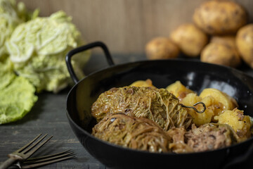 mit Hackfleisch gefüllte und Wirsing umwickelte Roulade auf dunklem Tisch aus Holz mit Kartoffeln als Beilage	