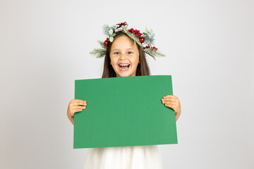 close-up portrait of laughing girl in Christmas wreath holding green paper isolated on white...
