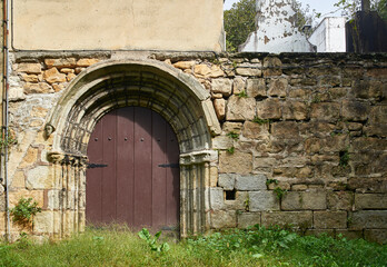 Fototapeta premium Antique Romanesque door on a rustic stone wall of a historic building in a European village, with five decorated with archivolts and baquettes finished with theriomorphic faces.