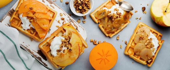 Delicious Belgian wafers with caramelized fruit, apple, banana, persimmon, pear and walnuts on a gray concrete or stone background. Ideas for breakfast. Selective focus. Top view. Place for text