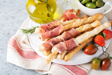Traditional Italian snacks for wine, breadsticks (grissini), tomatoes, prosciutto (jamon), strawberries and olives.