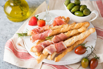 Traditional Italian snacks for wine, breadsticks (grissini), tomatoes, prosciutto (jamon), strawberries and olives.